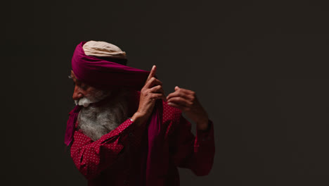 Fotografía-De-Estudio-Con-Iluminación-Tenue-De-Un-Hombre-Sikh-Mayor-Con-Barba-Atando-Una-Tela-Para-Hacer-Un-Turbante-Contra-Un-Fondo-Oscuro